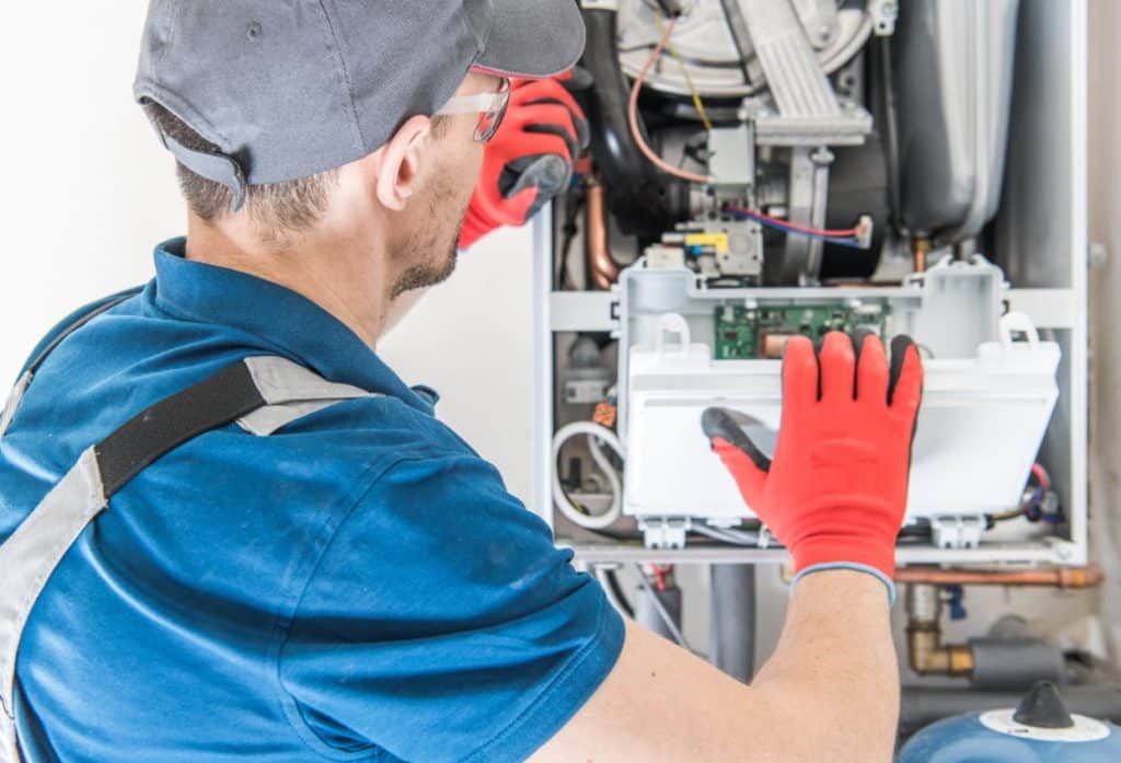 HVAC technician wearing safety gloves inspecting the internal components of a residential furnace during a repair.